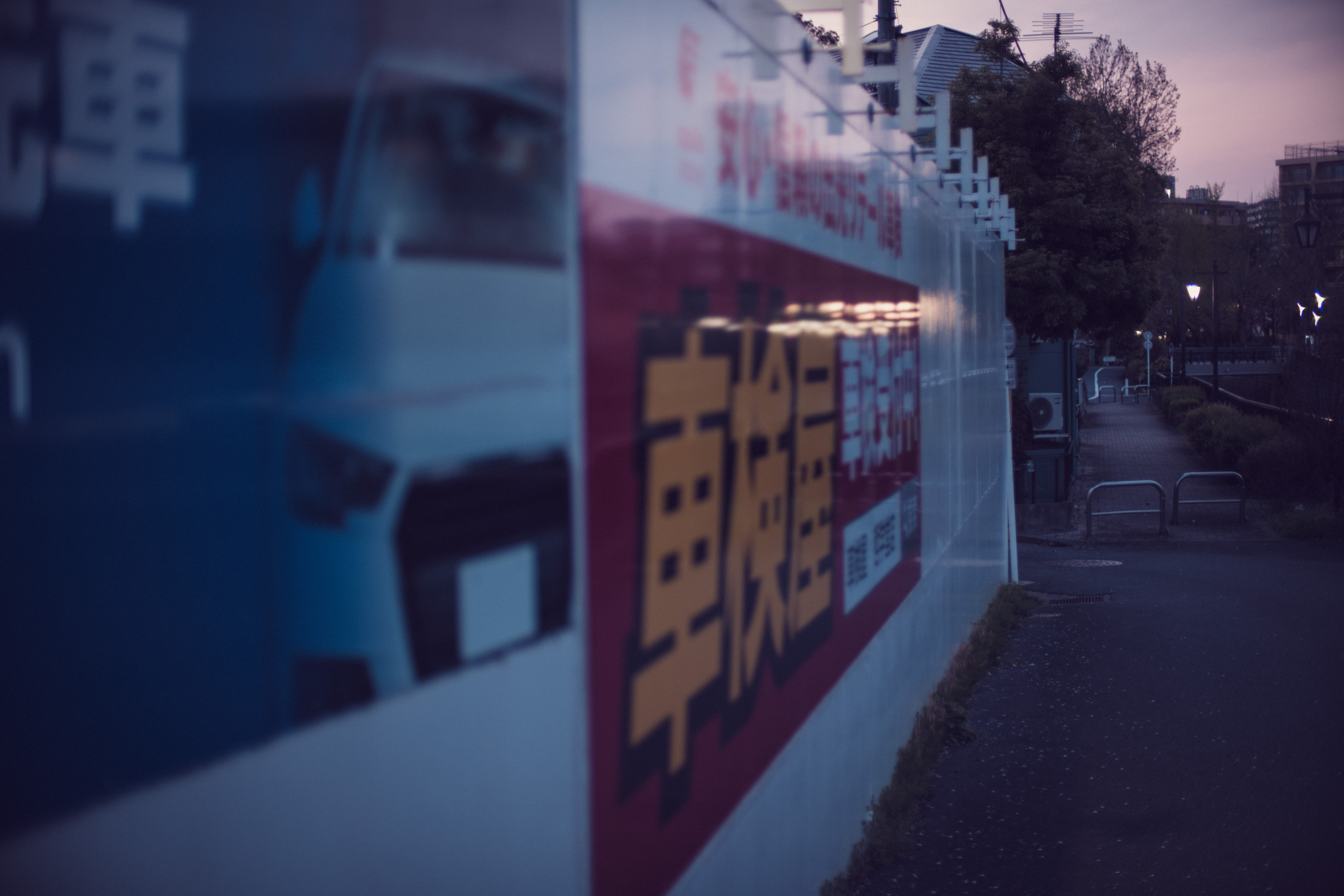A row of softly lit vending machines beside a quiet Tokyo path during the transition into blue hour