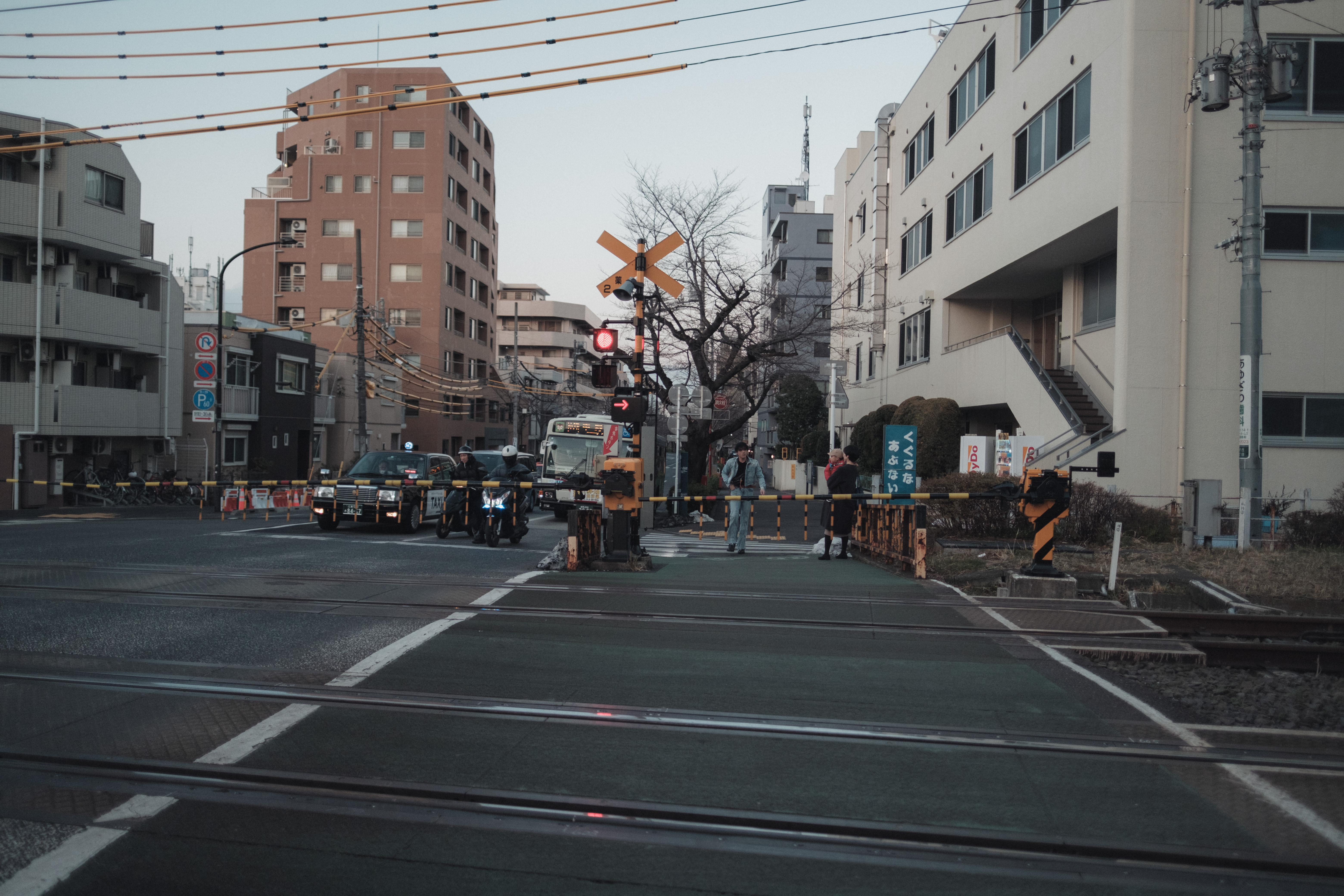 A dense Tokyo railroad crossing organized by rails, road lines, signals, vehicles, and distant pedestrians
