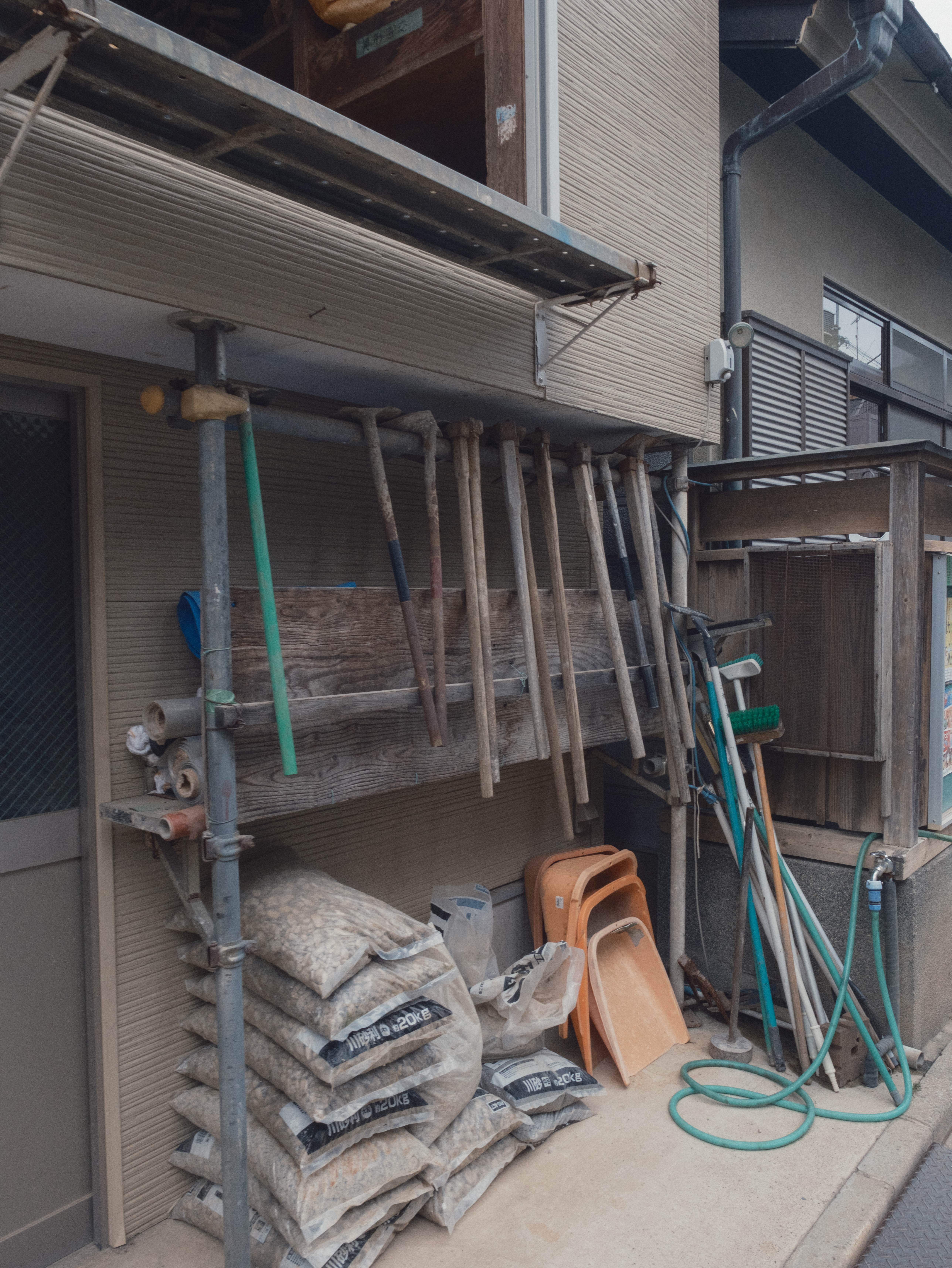 A Tokyo building exterior with visible supports, tools, and repair materials, photographed without turning the intervention into a metaphor