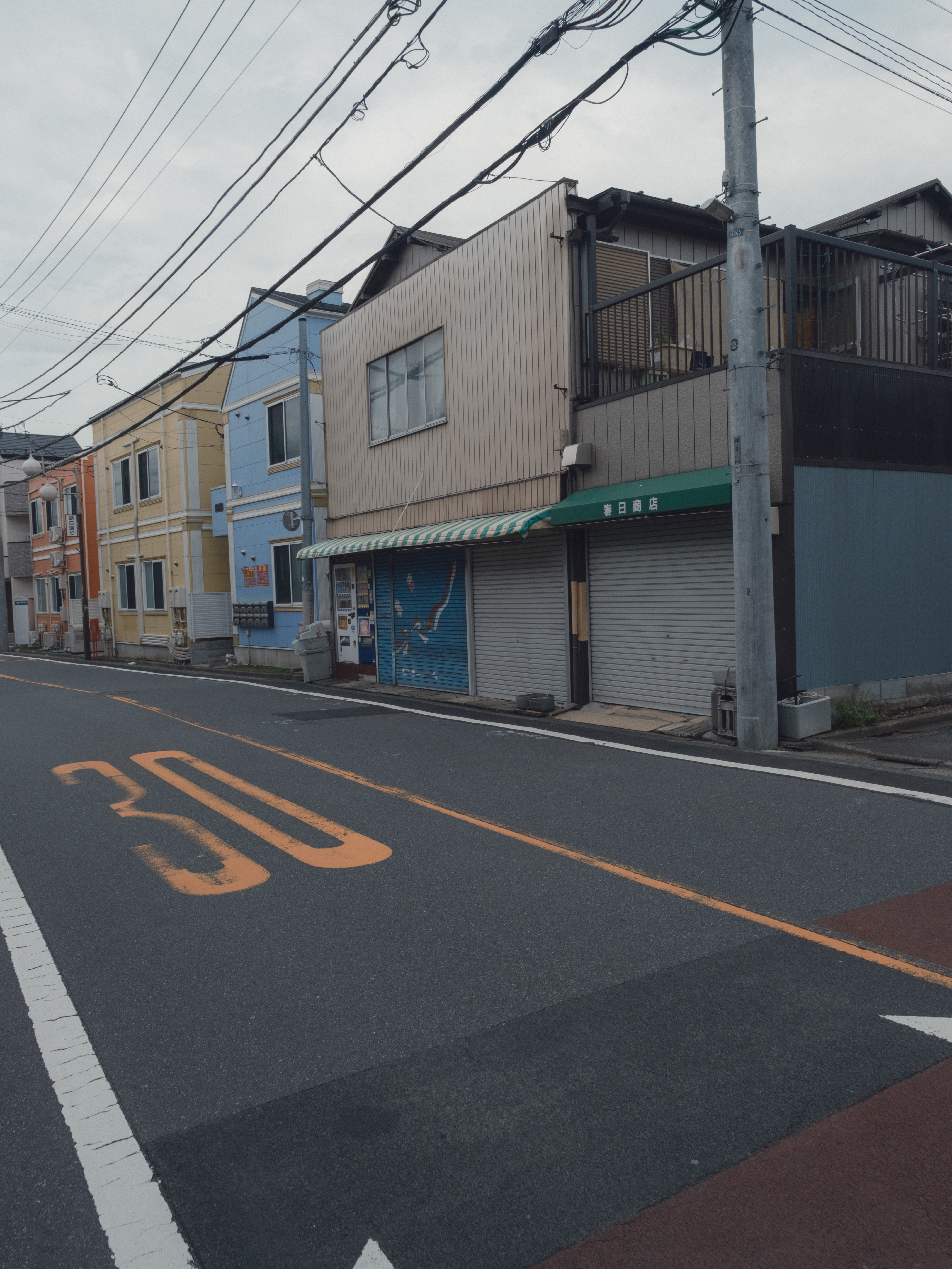 A quiet Tokyo street where pale yellow, blue, green, and orange appear together under overcast light